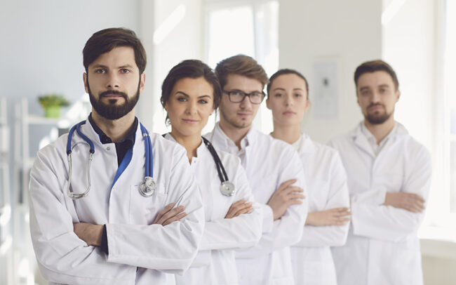 A group of confident practicing doctors cross arms in white coats are smiling in the clinic.