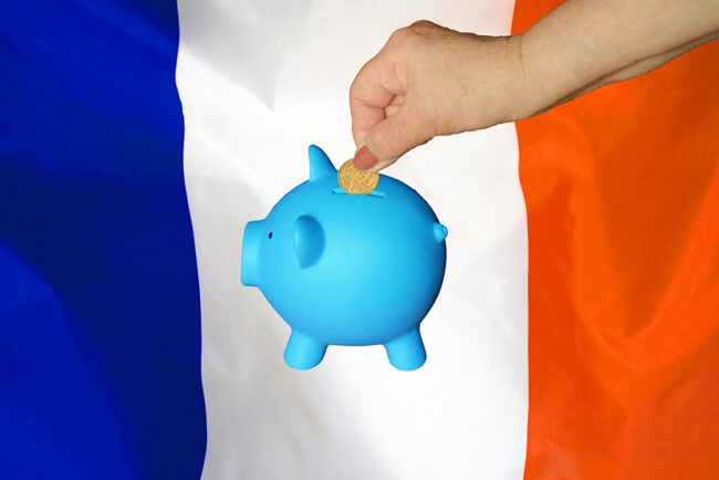 Hand putting coin to piggy bank on France flag background