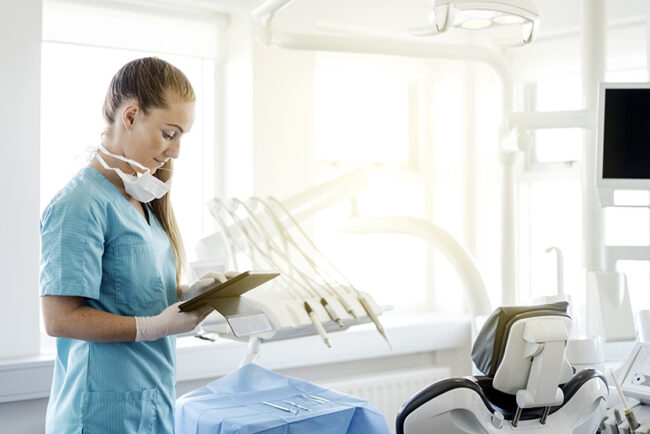 Dentist using digital tablet by chair in clinic