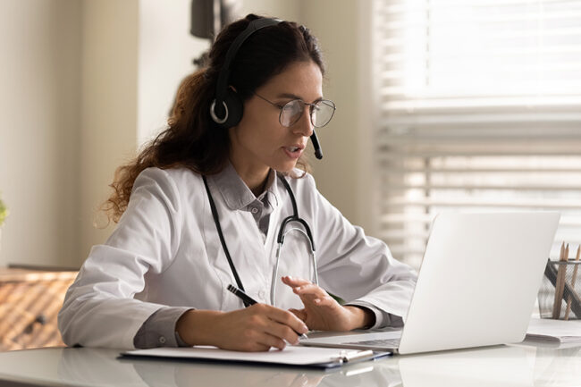 Focused young female doctor in headset watching webinar taking notes