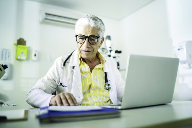 Senior male doctor using laptop at doctor’s office