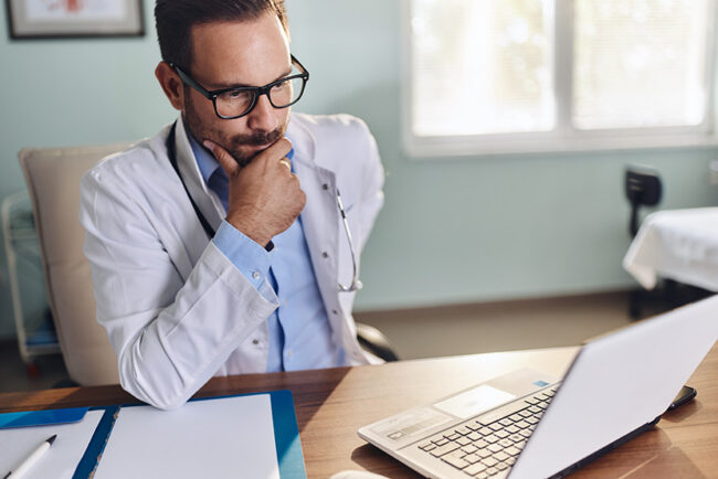 Thoughtful male doctor working on laptop in the office.