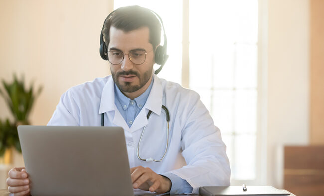 Focused young male doctor in headphones learning using computer app.