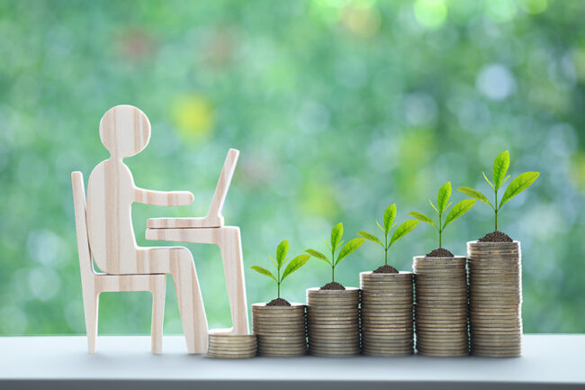Investment and business concept,Man using laptop computer with trees growing on stack of coins money on natural green background,Investors strategy