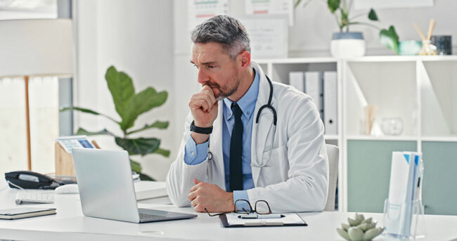 Shot of a mature doctor sitting alone in his clinic and looking contemplative while using his laptop