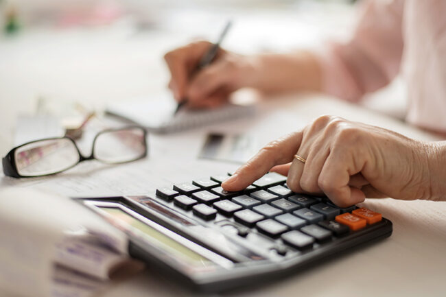 Pension calculation concept, old hands counting finances on a home calculator , close- up