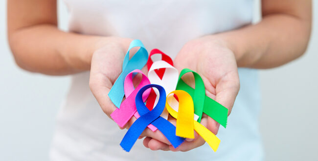 World cancer day, February 4. Hand holding blue, red, green, white, pink, navy blue and yellow ribbons for supporting people living and illness. Healthcare and Autism awareness day concept