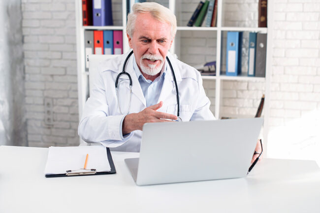 Senior male doctor with a stethoscpe using laptop